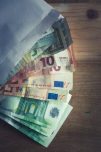 A collection of Euro banknotes emerging from an envelope on a wooden surface.