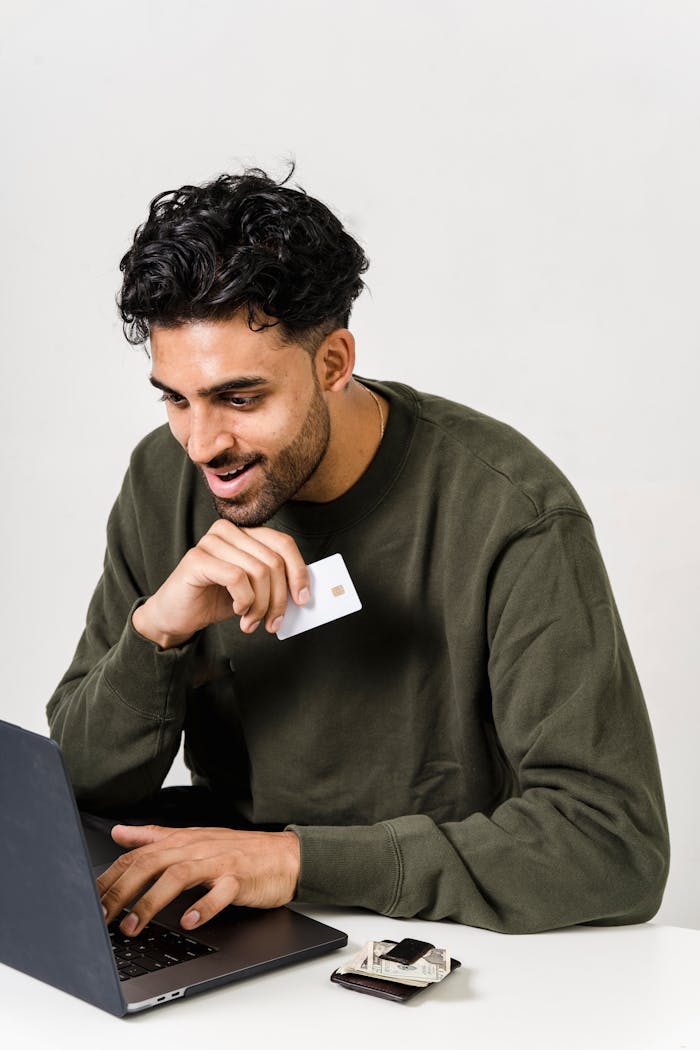 Man in green sweater uses laptop for online shopping, holding a credit card.