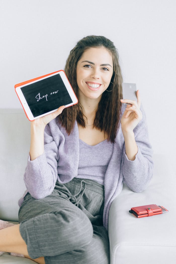 Young woman sitting on a couch holding a tablet and credit card, ready to shop online.